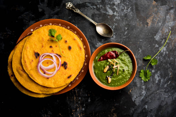 Stack of golden besan chilla (savory Indian pancakes) topped with onion rings and cilantro, served with a bowl of green chutney.