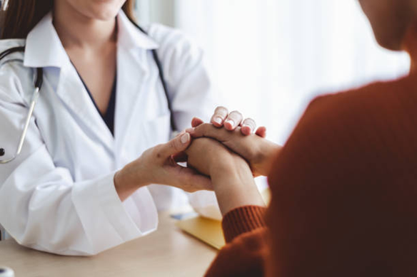 Doctor in a white coat gently holds a patient's hands in a comforting gesture during a consultation.