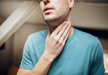 Man in a blue shirt touching his throat, indicating possible sore throat or discomfort.