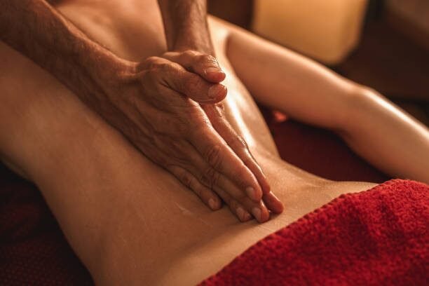 Hands massaging a person's back during a spa massage, with a red towel draped on the lower back.