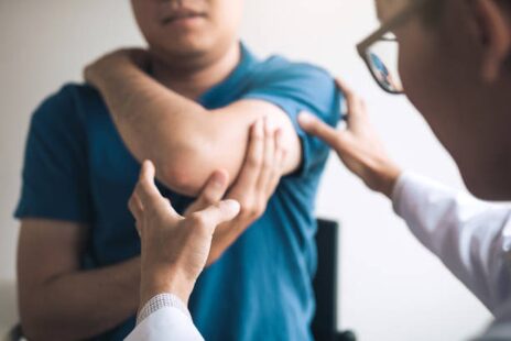 Medical professional examines a patient's arm at the shoulder, lifting the arm to assess movement.