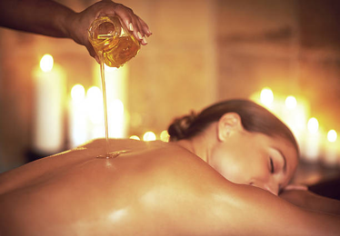 Person receives a candlelit spa massage as warm oil is poured along their bare back by a therapist.