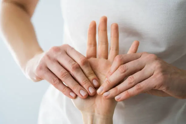 Caregiver gently supports a person’s hand with both hands in a comforting gesture.