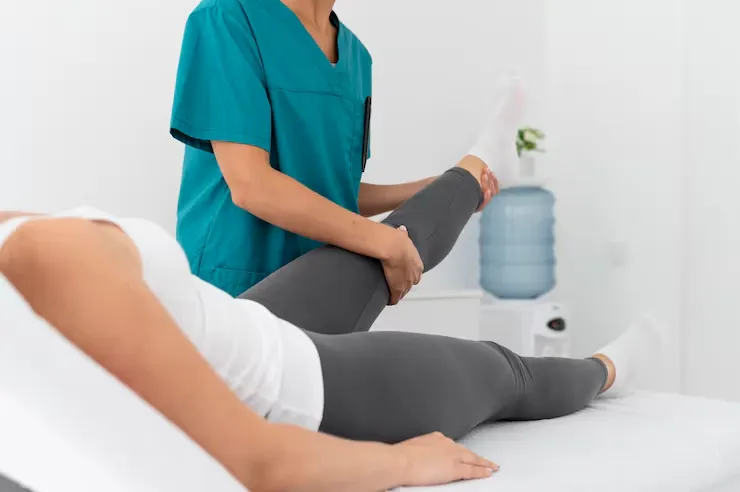 Healthcare professional in teal scrubs assisting a patient with a leg stretch on a treatment table
