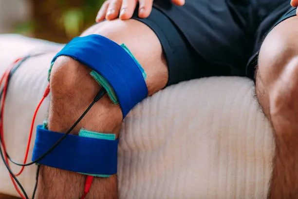 Knee undergoing rehabilitation with blue athletic tape and electrode wires for electrical stimulation therapy