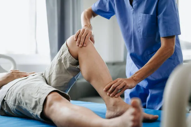Physical therapist in blue scrubs mobilizing a patient’s knee while the patient lies on a medical table