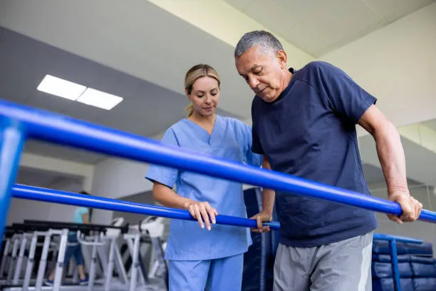 Therapist guiding an older man as he uses parallel bars for rehabilitation therapy in a clinic