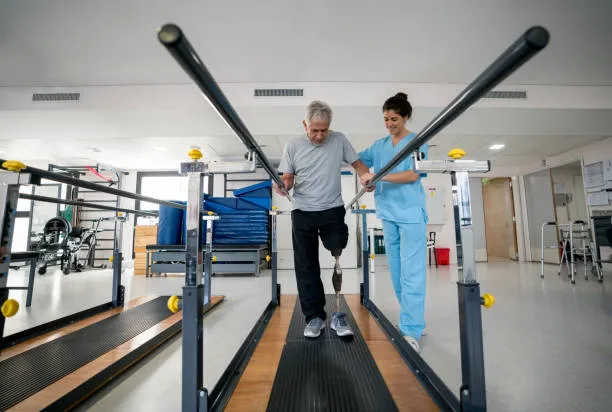 Man with a prosthetic leg walks on a parallel-bar treadmill as a clinician guides him in a rehabilitation gym; supportive equipment visible in the background.